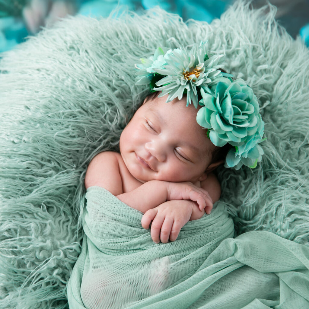 Newborn photography session of a little girl smiling while sleeping posed on soft green blanket