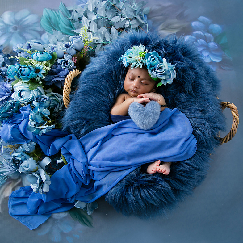 Newborn photography session of a baby girl posed in a basket surrounded by flowers.